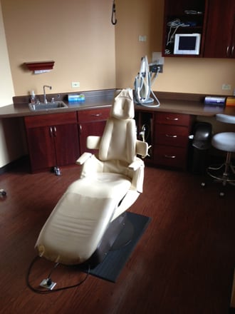 A vertical shot of a clinical dental operatory showing the patient chair, sink area, and wall-mounted monitors.