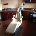 A vertical shot of a clinical dental operatory showing the patient chair, sink area, and wall-mounted monitors.