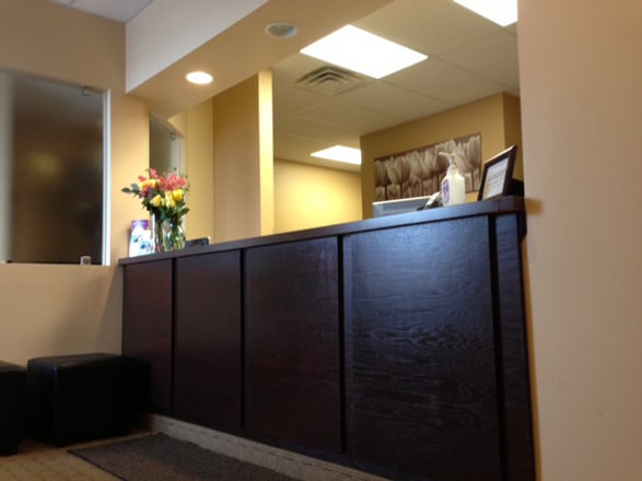 A professional dental reception desk made of dark wood with warm overhead lighting and a bouquet of flowers on the counter.