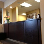 A professional dental reception desk made of dark wood with warm overhead lighting and a bouquet of flowers on the counter.