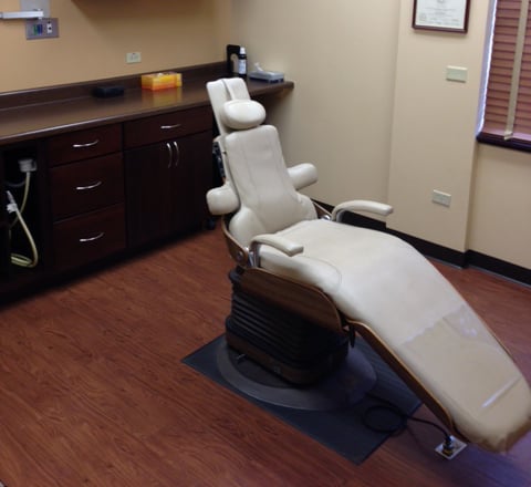 A modern dental treatment room featuring a reclining beige patient chair and dark wood cabinetry for medical tools.