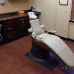 A modern dental treatment room featuring a reclining beige patient chair and dark wood cabinetry for medical tools.