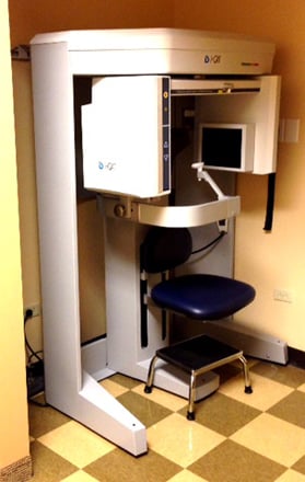 A specialized panoramic dental X-ray machine (CBCT) located in a dedicated imaging room with checkered flooring.