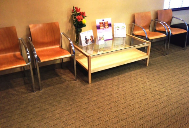 A dental office waiting area featuring orange leather armchairs and a glass coffee table with informational brochures.