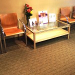 A dental office waiting area featuring orange leather armchairs and a glass coffee table with informational brochures.